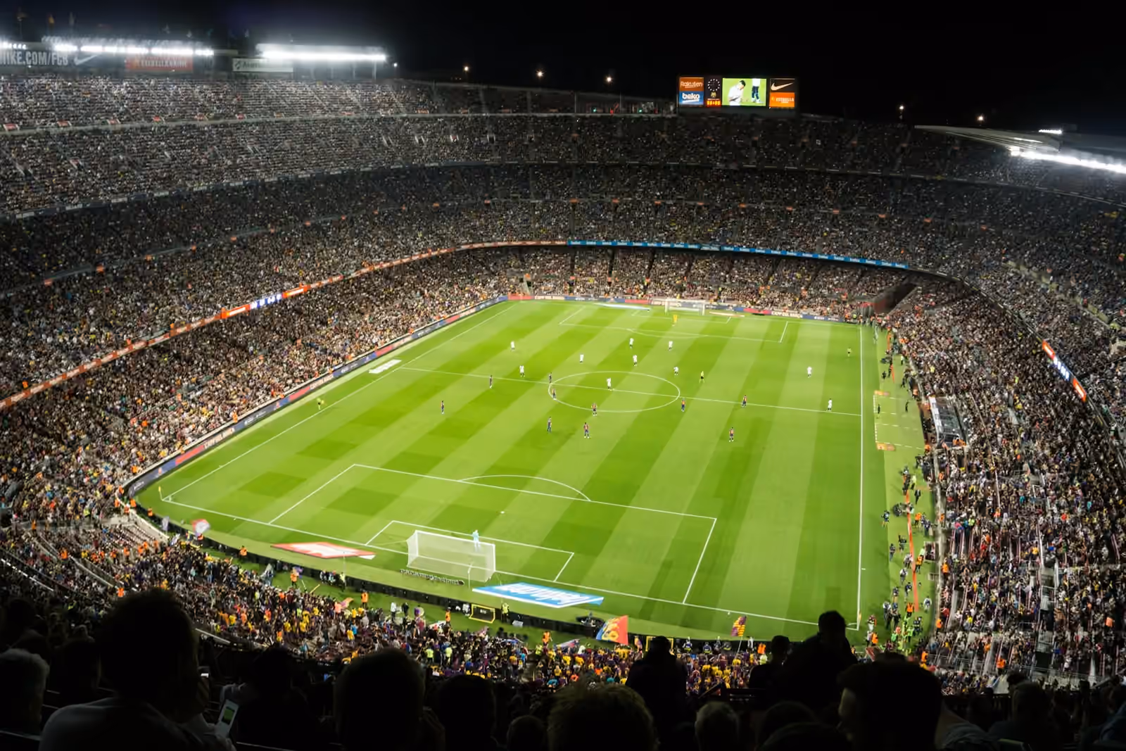Floodlit football stadium at night, seen from the stands